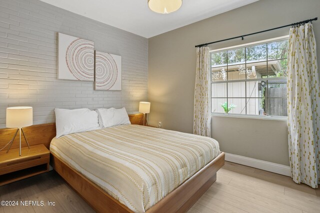 bedroom featuring light hardwood / wood-style flooring and brick wall