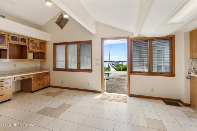 kitchen featuring vaulted ceiling with beams, built in desk, light tile patterned flooring, and baseboards