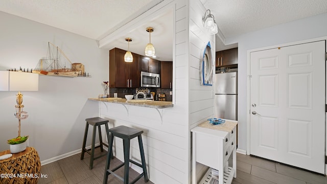 kitchen with a kitchen breakfast bar, decorative backsplash, a textured ceiling, dark brown cabinetry, and stainless steel appliances