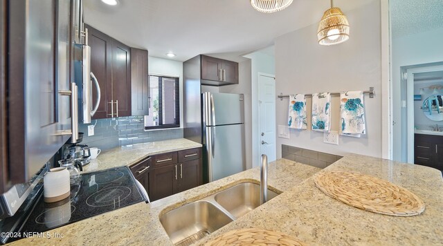 kitchen featuring light stone countertops, dark brown cabinets, sink, decorative light fixtures, and stainless steel refrigerator