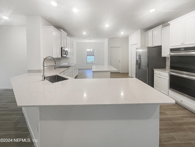 kitchen with stainless steel appliances, sink, white cabinetry, a center island, and light stone counters