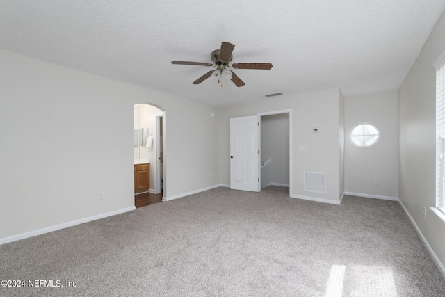 unfurnished bedroom with carpet, a textured ceiling, ensuite bath, and ceiling fan