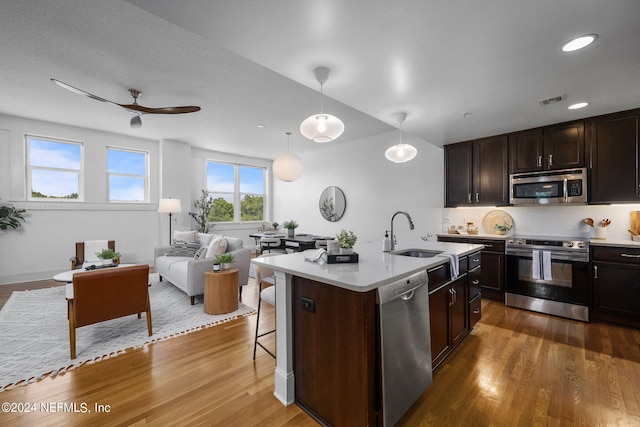 kitchen featuring a center island with sink, stainless steel appliances, hanging light fixtures, dark hardwood / wood-style flooring, and sink