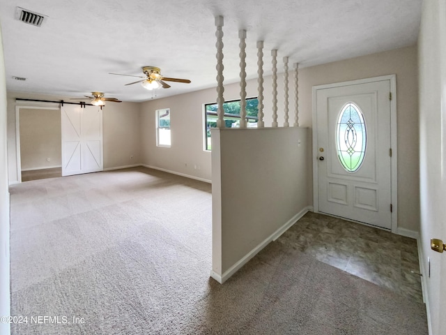 entryway featuring ceiling fan, a barn door, and carpet flooring