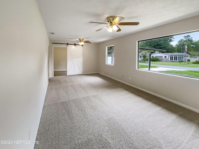 carpeted empty room featuring ceiling fan and a barn door