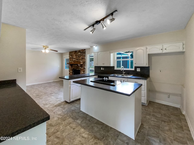 kitchen with black electric stovetop, kitchen peninsula, ceiling fan, white cabinets, and sink