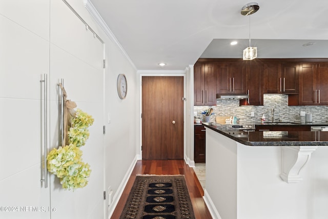 kitchen with sink, dark stone countertops, hardwood / wood-style floors, a breakfast bar area, and ornamental molding