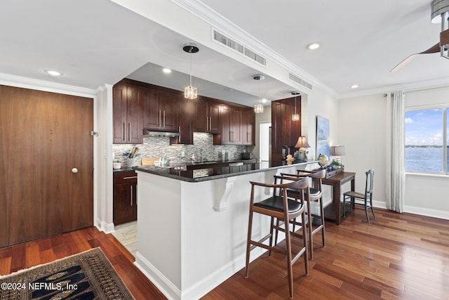 kitchen featuring pendant lighting, crown molding, light hardwood / wood-style flooring, kitchen peninsula, and a breakfast bar area