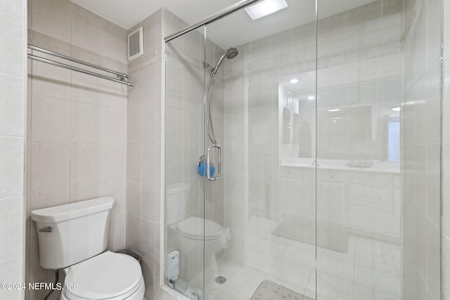 bathroom featuring a shower with door, toilet, and tile walls