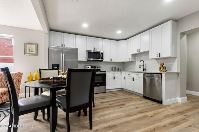 kitchen featuring white cabinets, decorative backsplash, light stone counters, stainless steel appliances, and light wood-type flooring