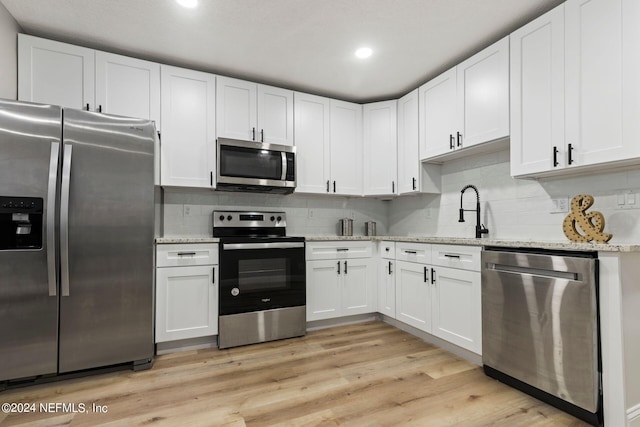 kitchen with appliances with stainless steel finishes, white cabinetry, tasteful backsplash, light stone countertops, and light hardwood / wood-style floors