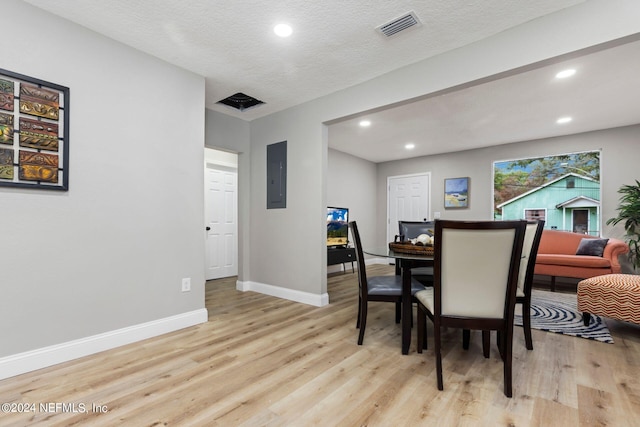 dining space featuring electric panel, light hardwood / wood-style floors, and a textured ceiling