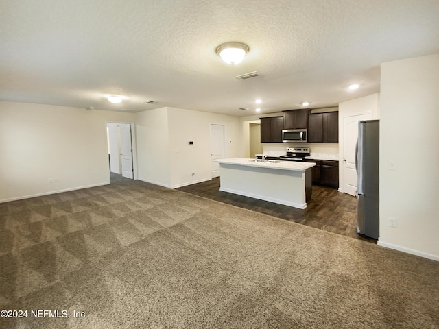 kitchen with dark colored carpet, appliances with stainless steel finishes, dark brown cabinets, and an island with sink