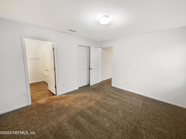 unfurnished bedroom featuring a textured ceiling, a closet, ensuite bath, and dark carpet