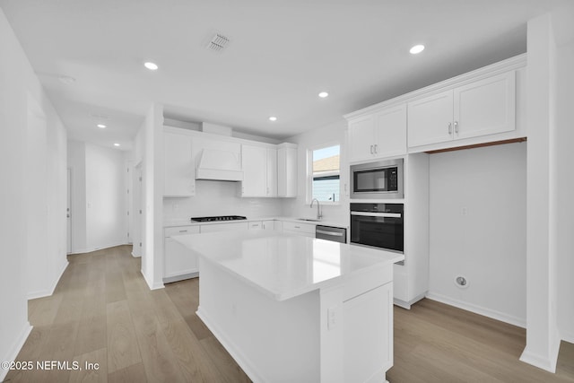 kitchen with a center island, black appliances, sink, light hardwood / wood-style flooring, and white cabinetry