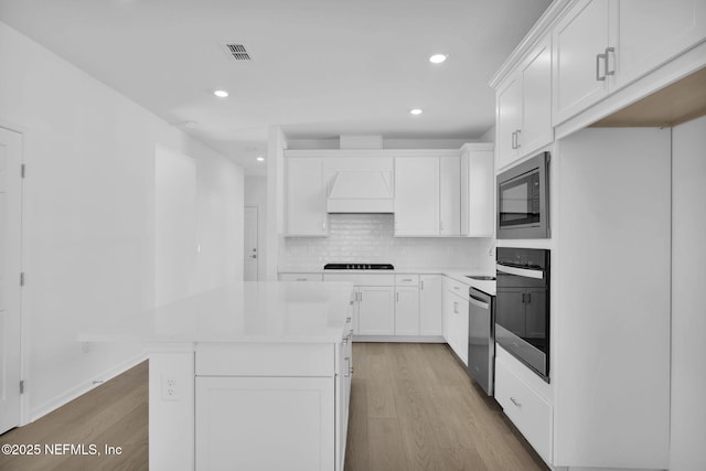 kitchen featuring a center island, white cabinetry, custom range hood, and appliances with stainless steel finishes