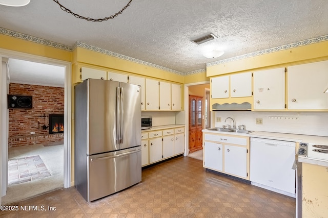 kitchen with a fireplace, stainless steel fridge, white dishwasher, and white cabinetry