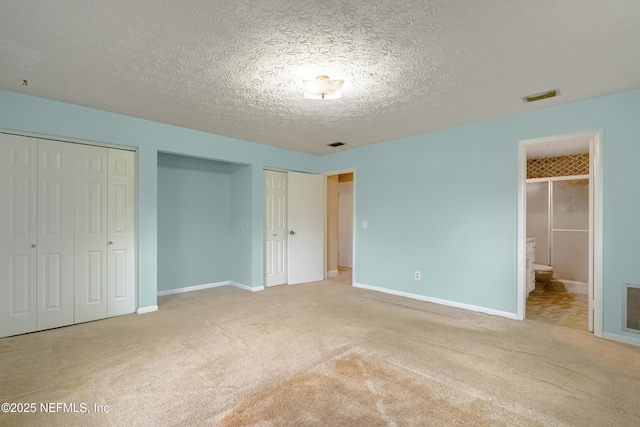 unfurnished bedroom featuring carpet, multiple closets, a textured ceiling, and ensuite bath