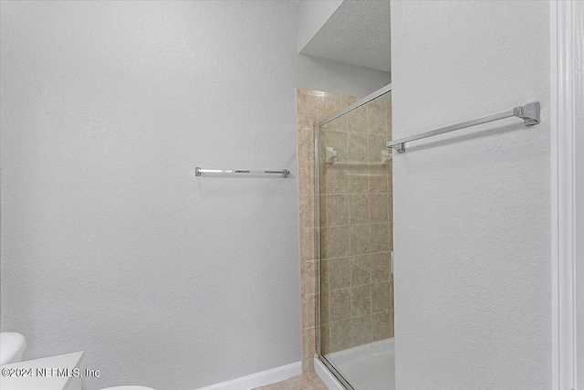 bathroom with a stall shower, baseboards, a textured ceiling, and toilet