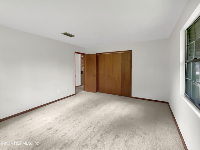 unfurnished bedroom with light colored carpet and a closet