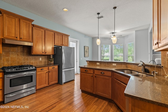 kitchen with sink, backsplash, stainless steel appliances, decorative light fixtures, and light wood-type flooring