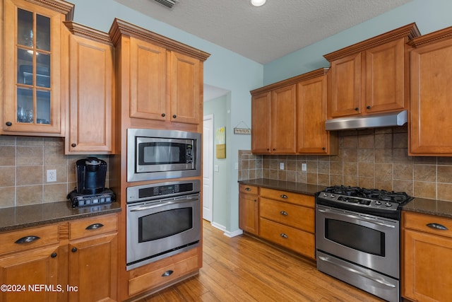 kitchen with tasteful backsplash, dark stone counters, stainless steel appliances, a textured ceiling, and light hardwood / wood-style flooring