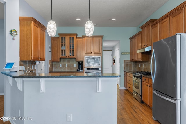 kitchen with hanging light fixtures, dark stone countertops, appliances with stainless steel finishes, and a breakfast bar area