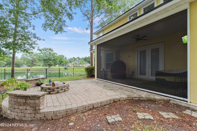 view of patio / terrace with a fire pit, a sunroom, ceiling fan, a water view, and french doors