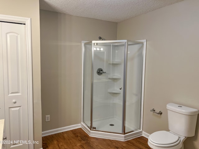 bathroom featuring hardwood / wood-style flooring, toilet, an enclosed shower, and a textured ceiling