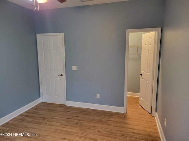 unfurnished bedroom with a walk in closet, light hardwood / wood-style flooring, a closet, and ceiling fan