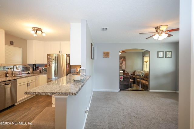 kitchen featuring light stone countertops, white cabinetry, kitchen peninsula, a breakfast bar area, and appliances with stainless steel finishes