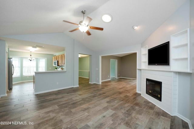 unfurnished living room featuring hardwood / wood-style floors, vaulted ceiling, ceiling fan with notable chandelier, and built in features