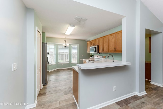 kitchen featuring kitchen peninsula, stainless steel appliances, light hardwood / wood-style floors, a notable chandelier, and decorative light fixtures