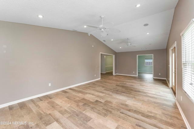 spare room with light hardwood / wood-style flooring, a textured ceiling, lofted ceiling, and ceiling fan