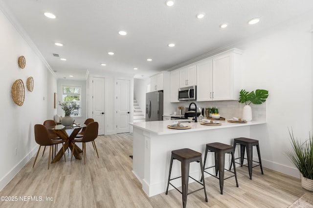 kitchen with white cabinetry, a kitchen breakfast bar, kitchen peninsula, decorative backsplash, and appliances with stainless steel finishes