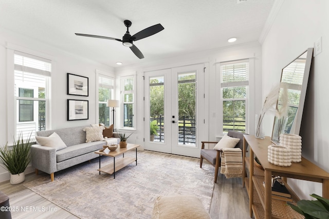 sitting room featuring french doors, light wood-type flooring, ceiling fan, and ornamental molding