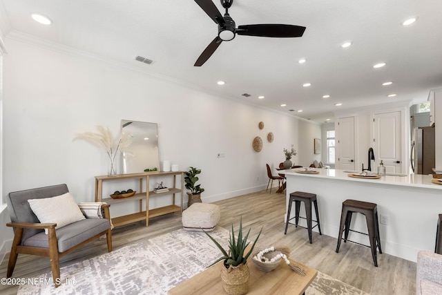 living room with ceiling fan, light hardwood / wood-style flooring, crown molding, and sink