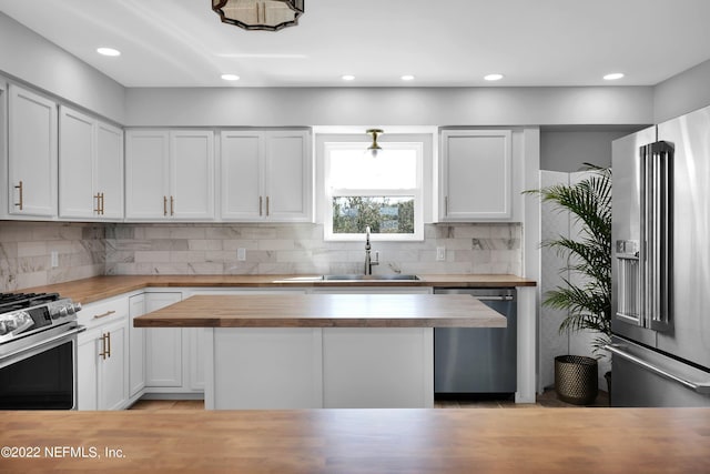 kitchen with butcher block counters, stainless steel appliances, sink, white cabinetry, and tasteful backsplash