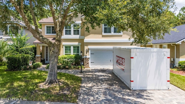 view of front facade featuring a garage, stone siding, decorative driveway, stucco siding, and a front lawn