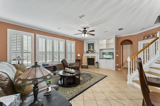 tiled living room featuring built in shelves, a textured ceiling, crown molding, and ceiling fan