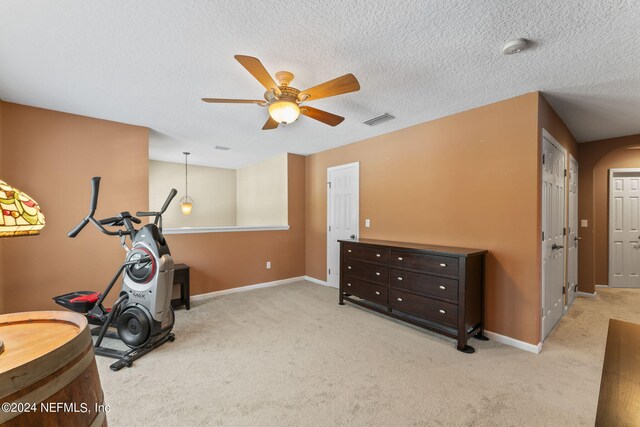 workout room with a textured ceiling, light colored carpet, and ceiling fan