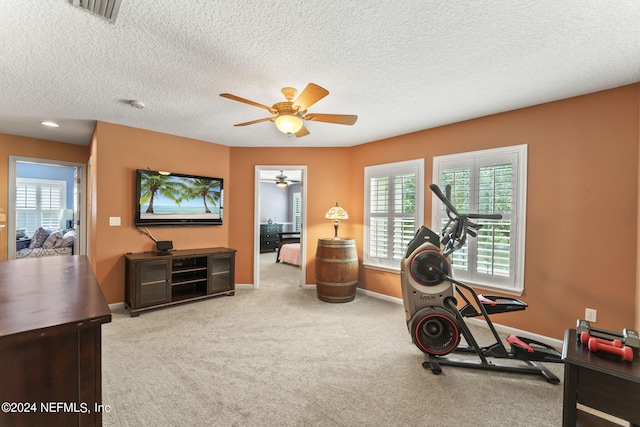 exercise area with light colored carpet, a textured ceiling, and ceiling fan