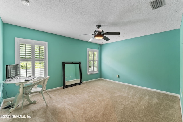 unfurnished office featuring light carpet, ceiling fan, and a textured ceiling