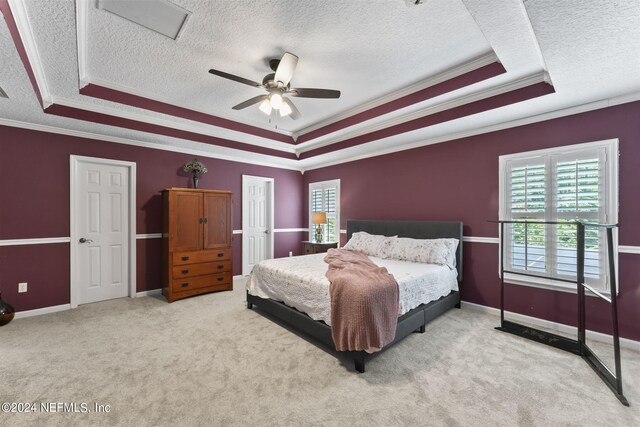 carpeted bedroom with ceiling fan, crown molding, and a tray ceiling