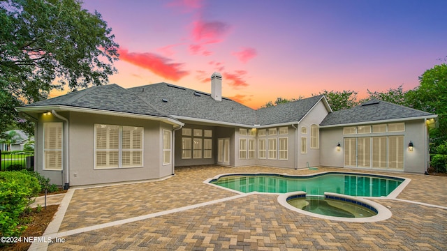 pool at dusk with an in ground hot tub and a patio