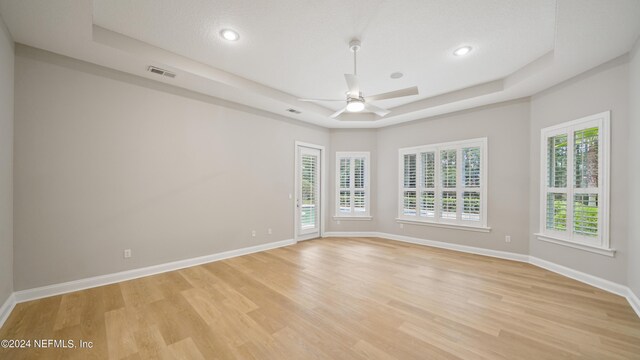 spare room featuring ceiling fan, light hardwood / wood-style floors, a textured ceiling, and a tray ceiling