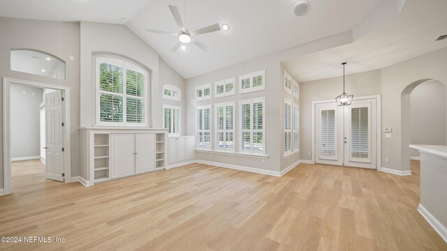 unfurnished living room with lofted ceiling, french doors, ceiling fan with notable chandelier, and light wood-type flooring