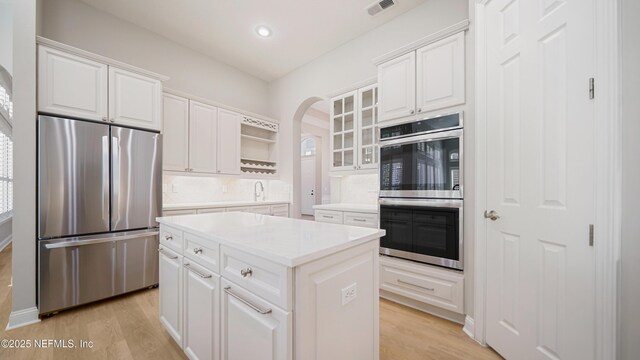 kitchen with backsplash, a kitchen island, appliances with stainless steel finishes, light hardwood / wood-style floors, and white cabinetry