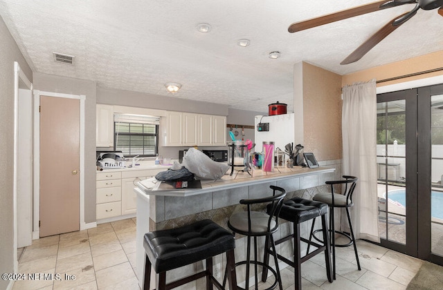 kitchen with kitchen peninsula, ceiling fan, a kitchen breakfast bar, and white cabinets