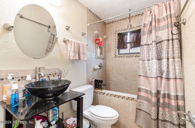 bathroom with sink, toilet, a textured ceiling, and tile walls